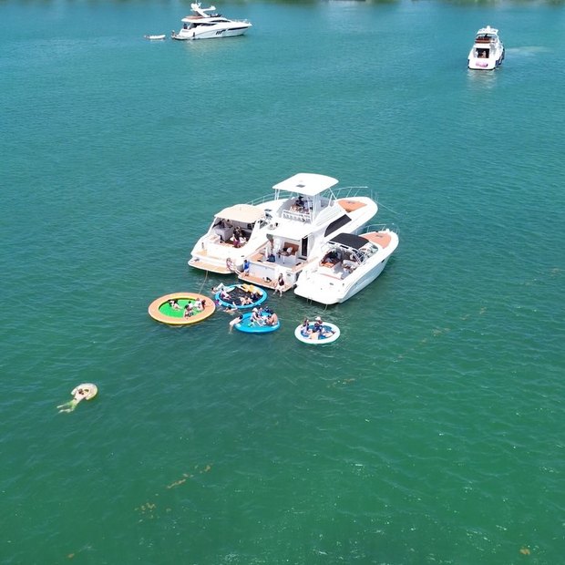 Two LuxSea boats rafted together on turquoise water with floating pools tied alongside, seen from above