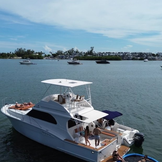 The Chris Craft anchored off a tree-lined shore with guests down on the swim platform